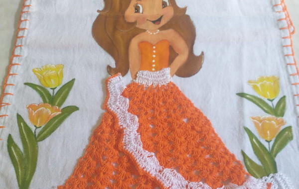 Uma boneca de crochê com roupa laranja e segurando abóboras